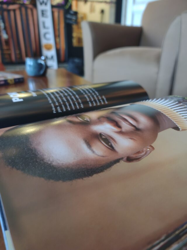 Open book on a table with a photo of a person, in a cozy reading area with a "Welcome" sign in the background.